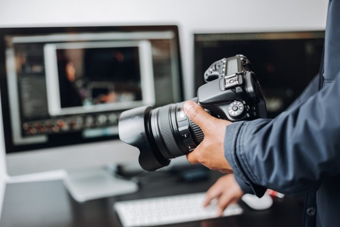 photographer's hand on their camera and a computer on a desk