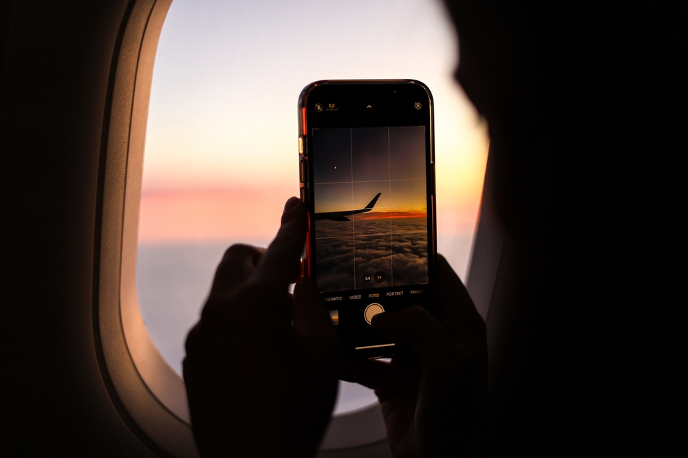 woman taking smartphone photo out of plane window
