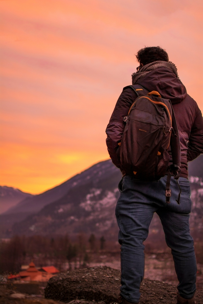 Man with a backpack standing on a mountain at sunset