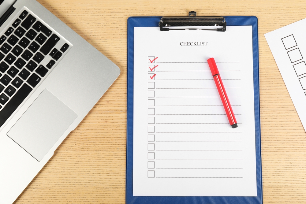Checklist with checkboxes, marker and laptop on wooden table