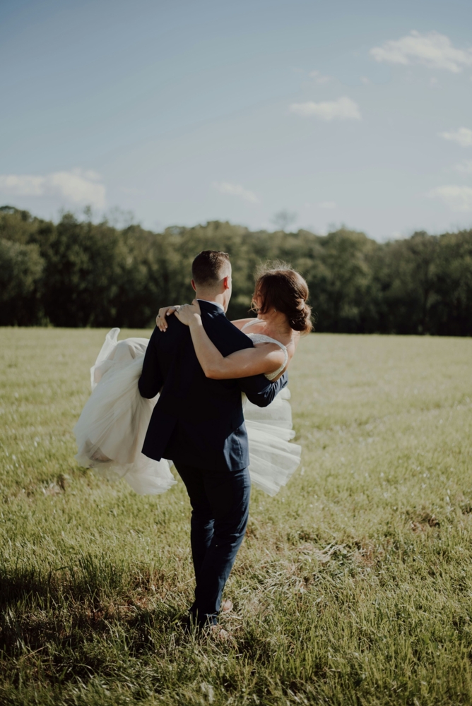 Groom carrying bride across a field