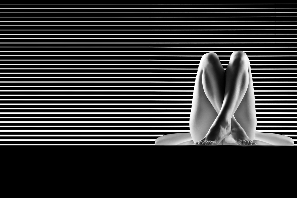 nude woman lying infront of striped background both her knees up and ankles crossed