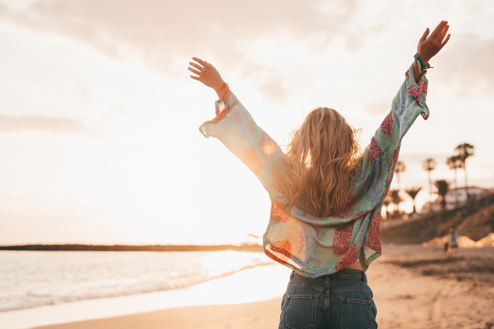 woman walking the beach with her arms raised