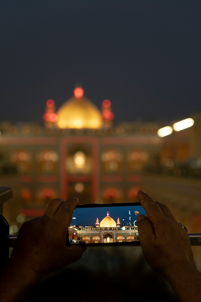 Hands holding phone capturing illuminated building at night Holy shrine of Imam Ali pbuh