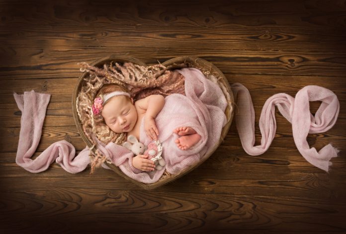 Newborn wrapped in pin in a heart basket with fabric spelling out love