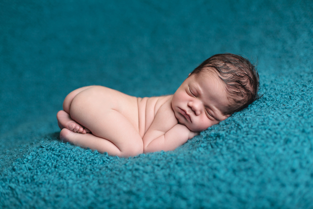 baby sleeping curled up on a blanket with butt up in the air