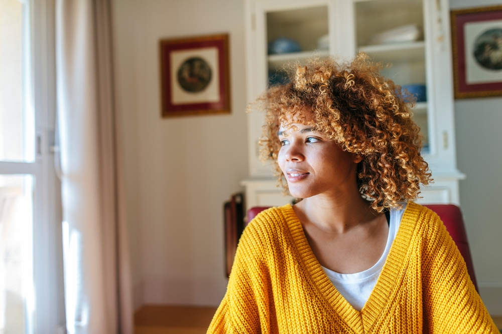 woman with curly hair wearing a yellow sweater sitting in her living room