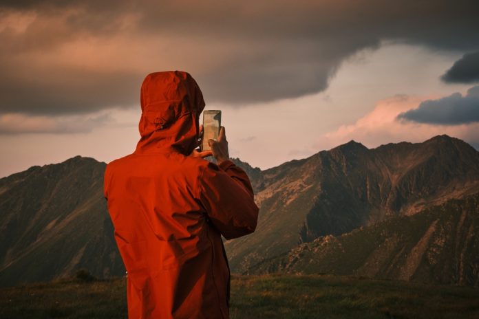 Person in red jacket taking a photo of mountains with a smart phone