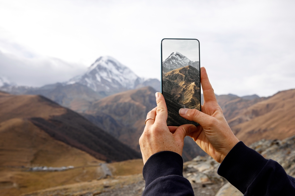 hands hold a smartphone capturing a mountain landscape