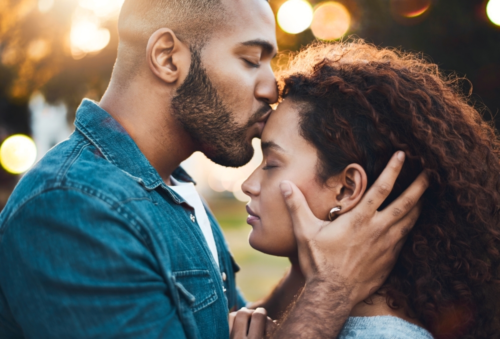 Man kissing woman on her forehead in the park, bokeh