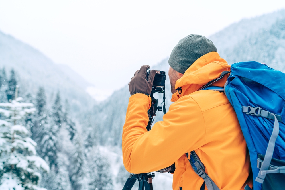 photographer using a digital camera and tripod while trekking winter mountains