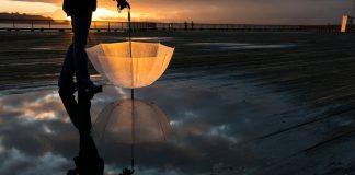 Bright umbrella held by a person reflected in a puddle at sunset