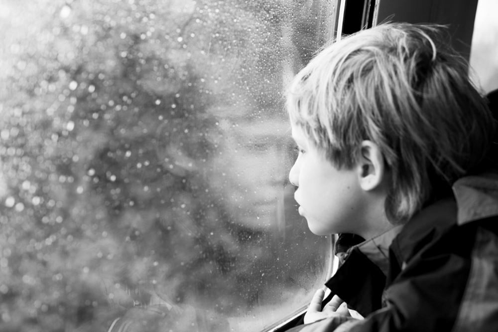 Boy looking out a window with his reflection