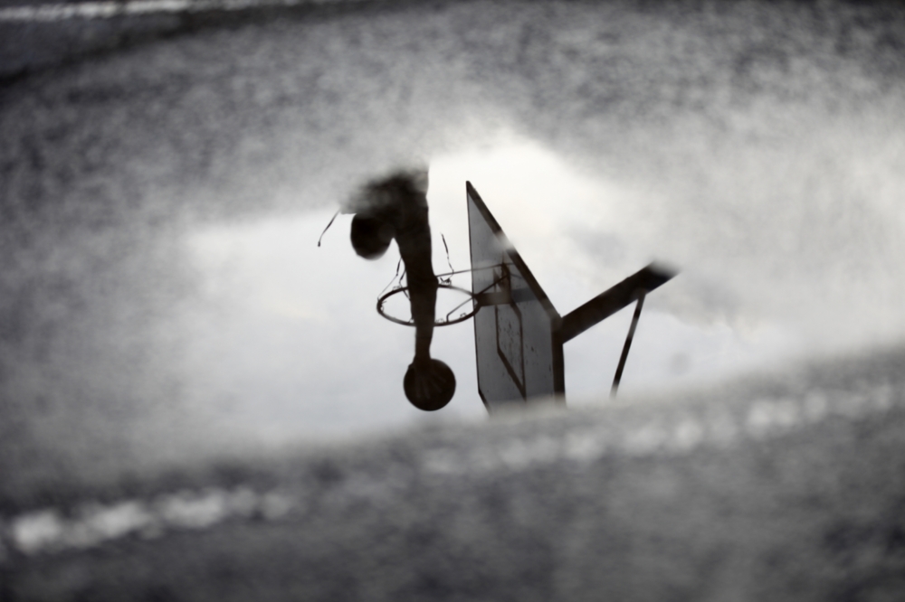 Man playing basketball reflected in a puddle