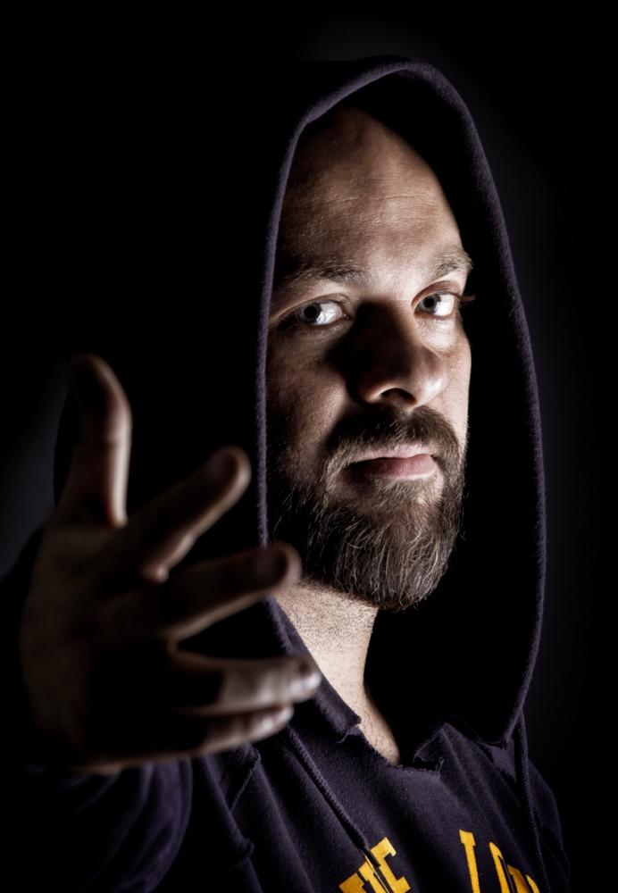 Low key portrait of a man wearing a hood and reaching toward the camera