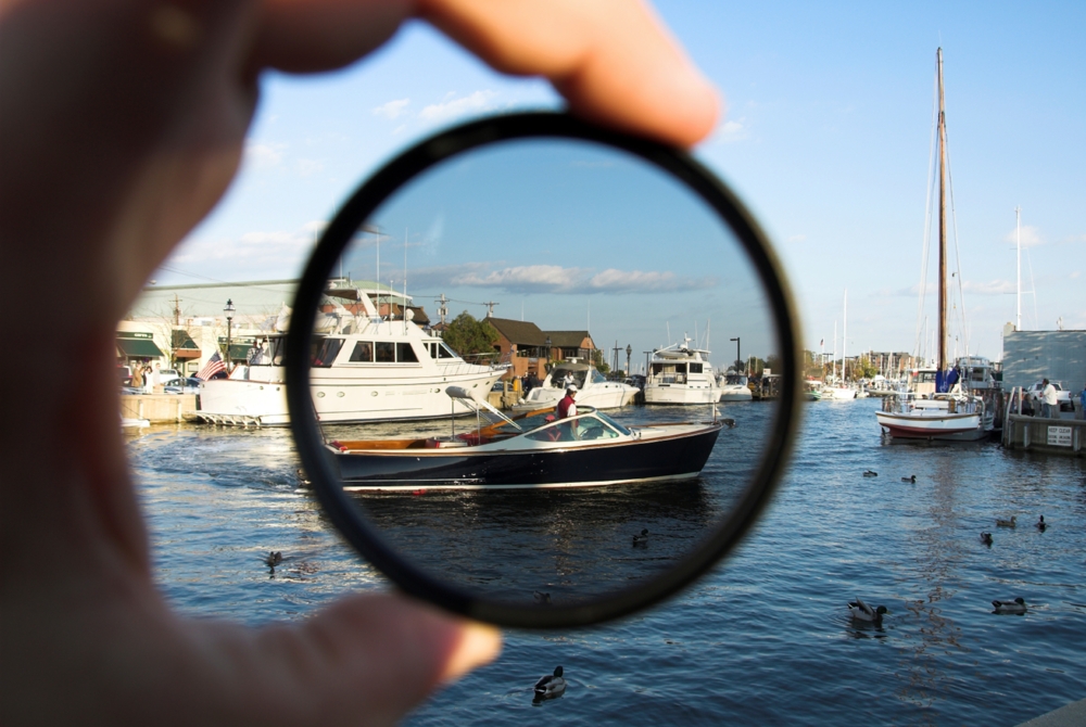 person holding a polarizing filter looking at boats