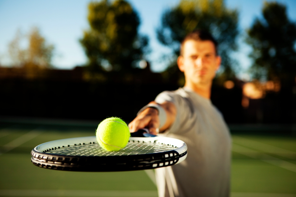 Man holding out a tennis racket with a tennis ball on it shallow depth of field