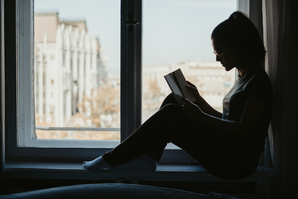 Silhouette of a girl with glasses reading book in the window
