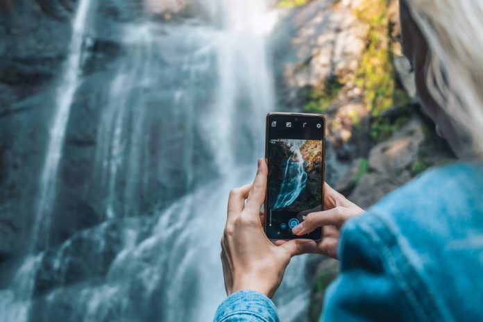 woman using smartphone to photograph waterfall