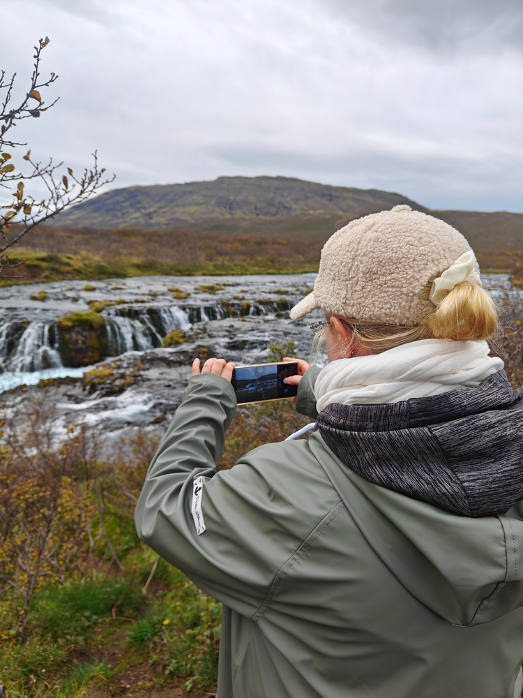 woman using smartphone to photograph waterfall in the rain