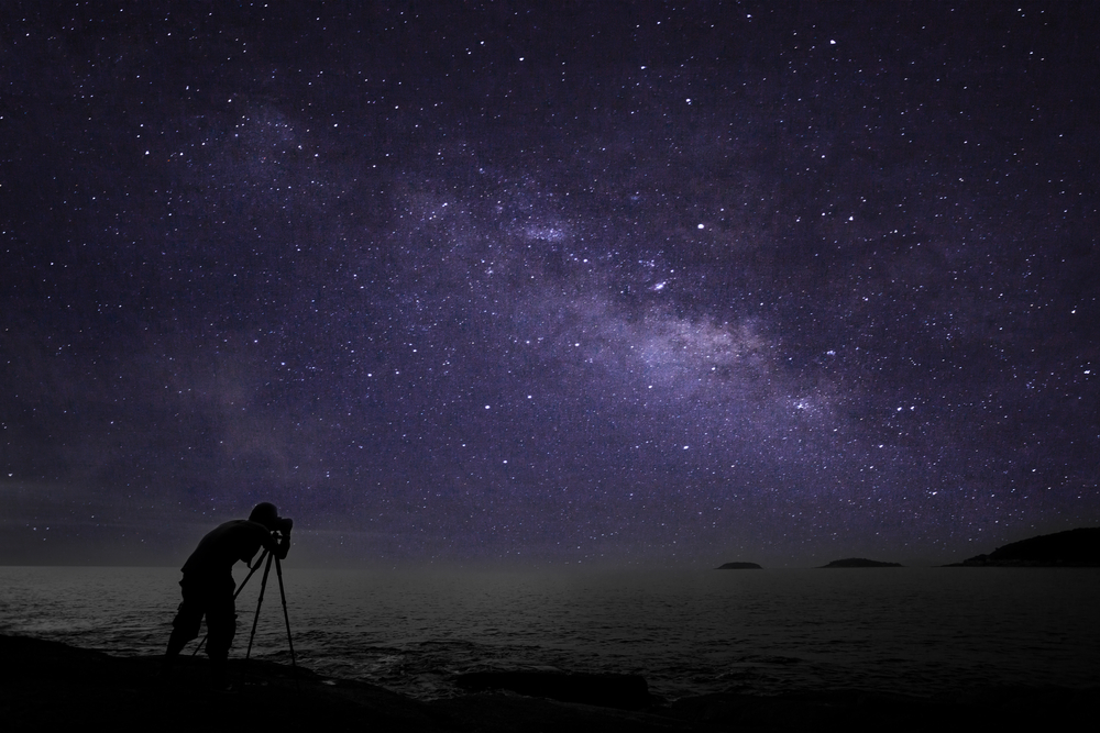 Astrophotographer manually focusing a camera on the Milky Way over the coast at night